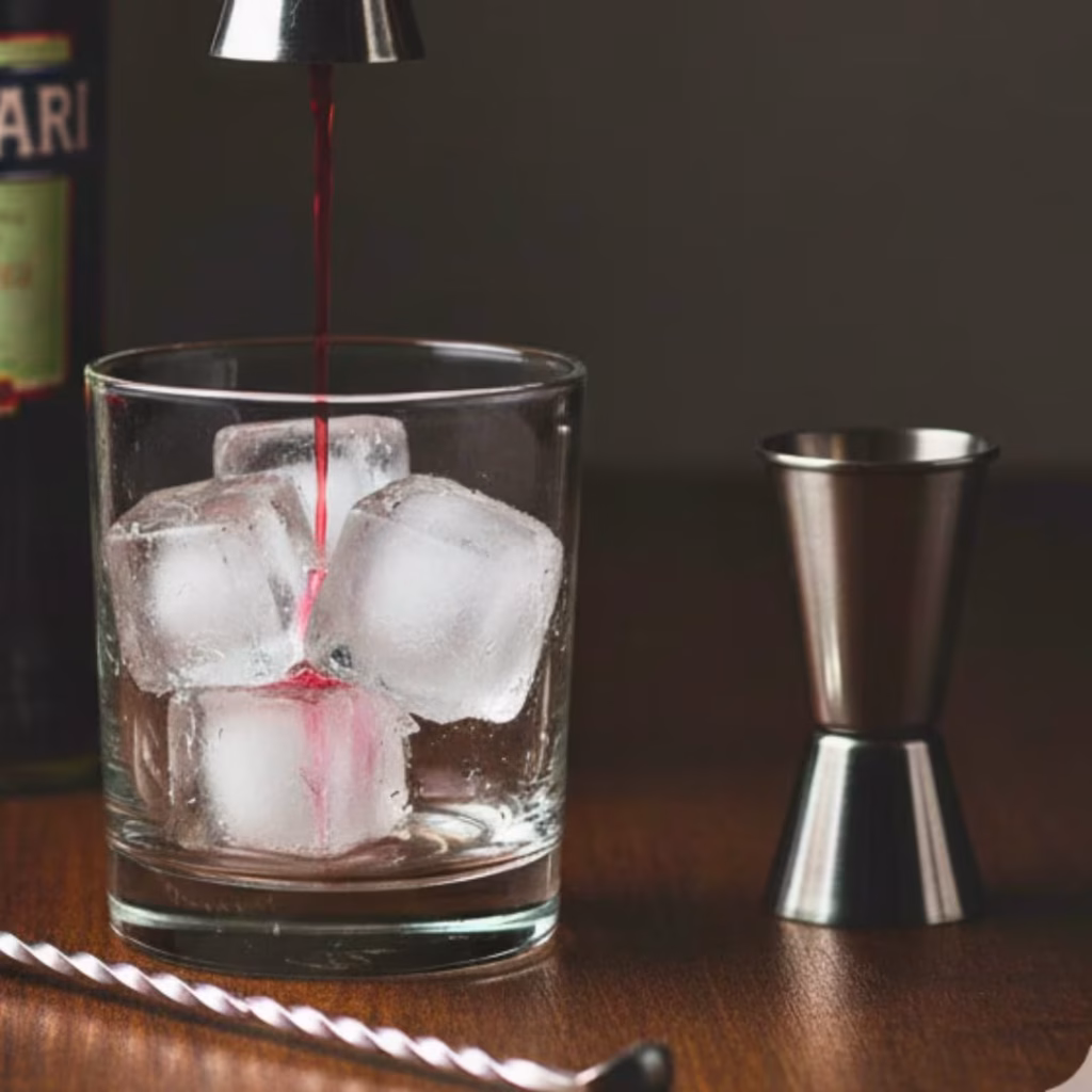 Measured jiggers of gin, Campari, and sweet vermouth